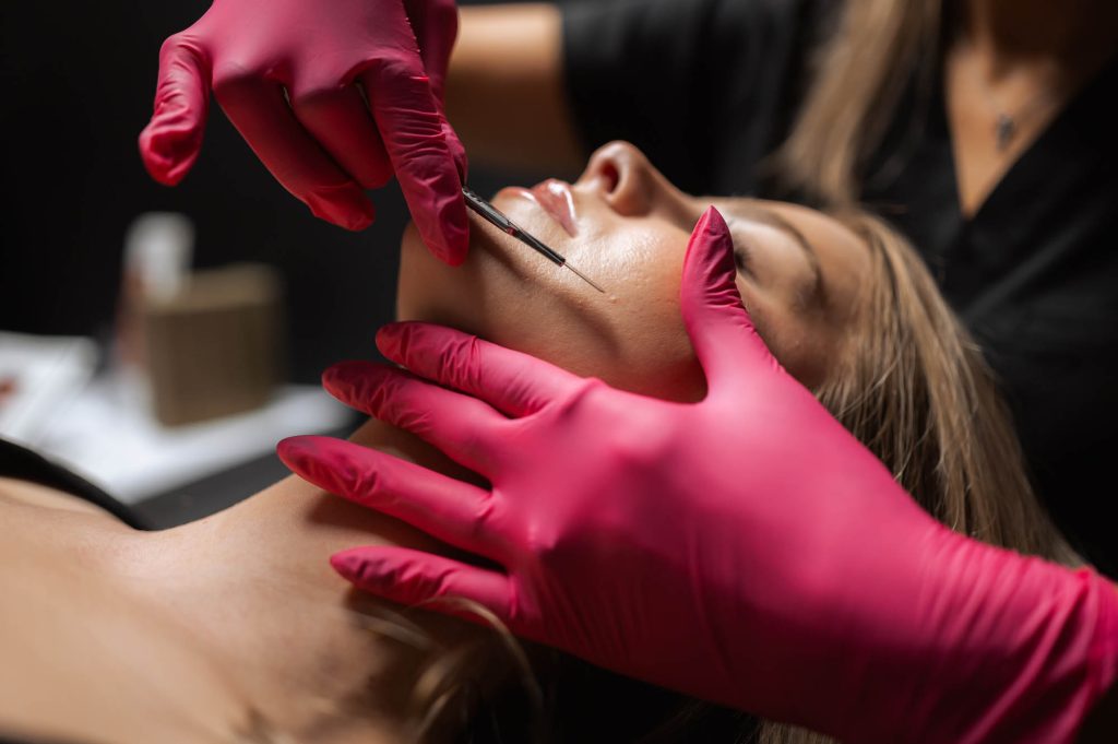 esthetician holding dermaplaning tool with pink gloves on woman's face at Ageless Aesthetics in Indianapolis